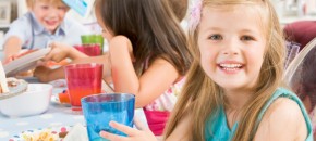 Young girl at party sitting at table with food smiling